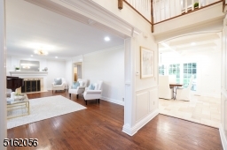 Foyer is double-height and features an open staircase, hardwood floors, chandelier, wainscoting, deep base and crown moldings