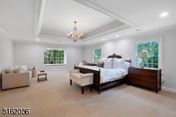 Primary Suite features a tray ceiling with a chandelier and recessed lights, wall to wall carpeting with hardwood floors underneath, three exposures of windows including a boxed window seat