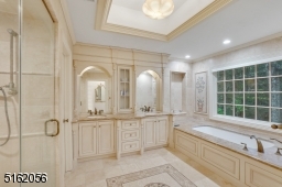 Primary Bathroom featuring pocket doors, marble floors with a mosaic decorative design, soaking jetted tub, double vanity with built-ins and extensive millwork, glass enclosed shower and a separate commode room with a door