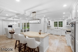 Chef's eat-in Kitchen featuring stone floors, coffered ceiling, built-in speakers, recessed lights, two built-in wall units with open shelving and cabinetry, island with stone counters and seating for three.