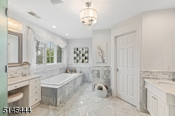 Primary Bathroom features gray and white marble floors and walls, recessed lights,  a wall-to-wall marble vanity with two sinks +  dressing / vanity area,
