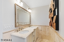 Full Hallway Bathroom with stone floors, double marble vanity, glass enclosed shower over tub and a separate commode room