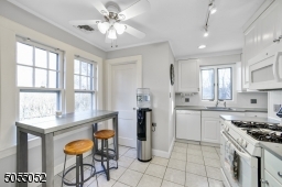Chef's Eat-In Kitchen featuring white tile floors, crisp white cabinetry, white appliances, pantry, ceiling fan with light, track lighting, recessed lighting, and double window overlooking the rear yard