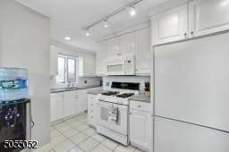 Chef's Eat-In Kitchen featuring white tile floors, crisp white cabinetry, white appliances, pantry, ceiling fan with light, track lighting, recessed lighting, and double window overlooking the rear yard