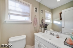 Powder Room with white vanity with under storage, recessed lights, and wall-to-wall mirror