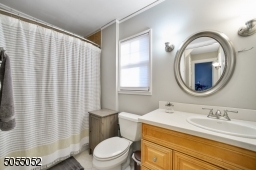 Full Hall Bathroom featuring a wood vanity with under storage, tile floor, dual sconces and a shower over a bathtub