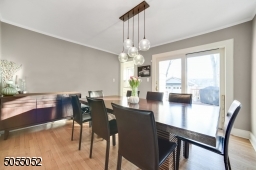 Dining Room featuring deep baseboard moldings, crown moldings, hardwood floors, modern chandelier and glass sliders to the large deck overlooking the level rear yard