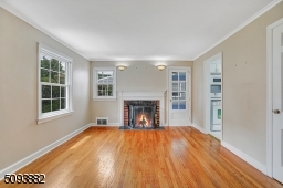 Spacious living room with crown molding, hardwood floors & wood-burning fireplace upon entrance.