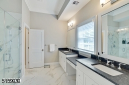 Primary Bathroom with marble floors, double vanities, glass enclosed shower and stone floors