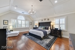 Primary Bedroom w/ hardwood floors, baseboard molding, large palladium window w/ plantation shutters, vaulted tray ceiling w/ molding, large WIC w/ window, built-in speakers, 2 chandeliers, built-ins & open shelving, sitting area / home office
