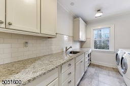 Laundry Room featuring stone floors, wall-to-wall built-in storage with granite counter and hanging storage, white subway tile backsplash, Whirlpool Duet Steam washer and dryer, 2 light fixtures and window overlooking rear yard
