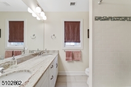 Full Hallway Bathroom featuring wood look tiles, wall to wall white double vanity with granite counter, floor to ceiling linen closet, two three light sconces, shower over tub with subway tiles and recessed light