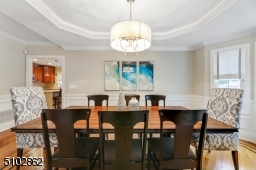 Dining Room featuring hardwood floors with walnut inlay border, crown moldings, wainscotting, modern chandelier, bay window, and recessed ceiling with back lighting