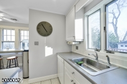 Chef's Eat-In Kitchen featuring white tile floors, crisp white cabinetry, white appliances, pantry, ceiling fan with light, track lighting, recessed lighting, and double window overlooking the rear yard