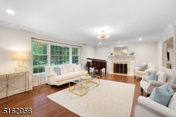 Living Room with hardwood floors, deep base and crown moldings, triple picture window, recessed and flush mount lights, built-in bar, fireplace with a white mantle and marble hearth