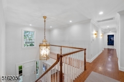 Open staircase with wainscoting and next to chandelier Hallway / landing overlooks the foyer and features a window, hardwood floors, deep moldings and two modern sconces