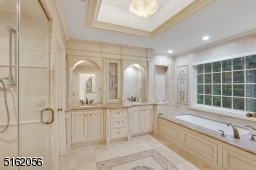 Primary Bathroom featuring pocket doors, marble floors with a mosaic decorative design, soaking jetted tub, double vanity with built-ins and extensive millwork, glass enclosed shower and a separate commode room with a door