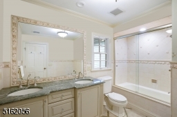 Full Hallway Bathroom with stone floors and walls, double vanity and a glass enclosed shower over tub