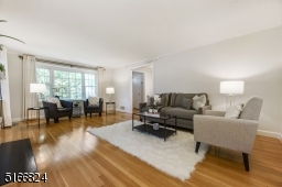 Living Room with a front-to-back view, hardwood floors, crown moldings, white wood fireplace flanked by two windows plus a triple window
