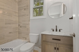 Bathroom with marble look tile floors, wood vanity with marble top, shower over tub with recessed light and three light sconce