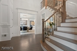 Double height Foyer featuring greige herringbone hardwood floors, crown moldings, paneled wall moldings, 2 coat closets, open staircase with decorative metal balusters and chandelier