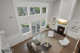 Great Room with hardwood floors, paneled walls, 21 ft coffered ceilings, recessed lights, fireplace with black granite surround and hearth flanked by floor to ceiling open shelving and lower cabinetry, double French doors and three architectural windows