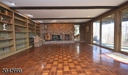 With parquet floors & brick fireplace, sliders to back patio, bar area, wall of shelves.