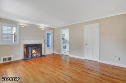 Spacious living room with crown molding, hardwood floors & wood-burning fireplace upon entrance.