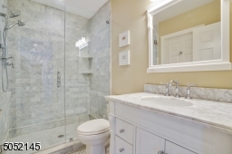 Full Bath featuring black and white basket weave marble floor, white vanity with grey and white marble top and frameless glass enclosed shower with grey marble subway tile