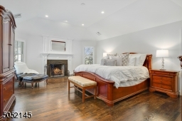 Primary Bedroom Suite featuring tray ceiling with recessed lights, hardwood floors, deep baseboard moldings, gas starter wood burning fireplace with white moldings flanked by two oversized windows