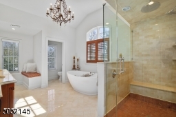 Primary Bathroom featuring marble floor, WoodMode double vanity & mirror flanked by built-ins, recessed lights, dual sconces, soaking tub, frameless glass walk-in shower w/ ?rain? shower head, heated towel rack, recessed lights & separate commode