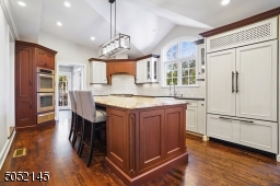 Gourmet Chef?s Eat-In Kitchen featuring WoodMode custom cabinetry, granite countertops, hardwood floors, crown moldings, recessed lights, modern light fixture over island, large island with seating and abundant storage, high-end appliances.
