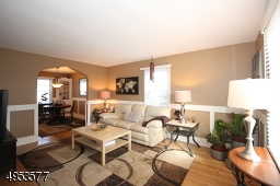 Living room features custom wainscotng, wood floors, and arched entryway to formal Dining Room