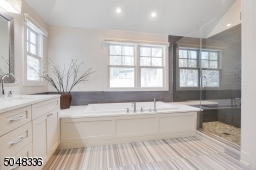 Primary Bathroom features vaulted ceiling, recessed lights, hanging chandelier, double sink vanity, stone floors, soaking tub with marble surround, seamless glass enclosed walk-in shower with built-in bench and private commode room w/ toilet