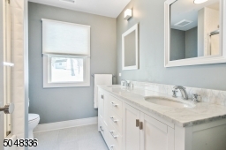 Hallway Bathroom features double sink wall-to-wall vanity with grey and white marble top and concealed under cabinet storage and shower over tub with sliding glass door and modern white textured tile
