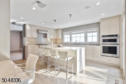 High-end appliances including KitchenAid double ovens, refrigerator, six-burner stove and Bosch dishwasher, undermount stainless steel sink with commercial style faucet and triple window overlooking rear yard, and built-in work space