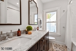 This well appointed full bathroom designed by Clear Space Home features a double vanity, marble countertops, Kohler plumbing, patterned hexagon tile, handmade-look subway tile and a large linen cabinet.