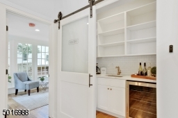 This walk-in pantry-bar area with barn door was designed by Clear Space Home with marble-look quartz, bar sink, beverage cooler, subway backsplash, satin brass hardware and tons of bonus storage.