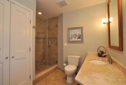 With Travertine marble flooring and vanity top, frameless shower, and storage closet
