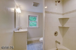 Adjacent bath features a tiled floor and shower-over-tub with decorative tile and corner niches.