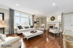 Living Room featuring hardwood floor, crown molding, baseboard moldings, designer pendant light fixtures, built-in speakers, Gas fireplace with elaborate wood mantle and travertine hearth.