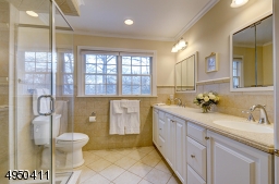 Features double sinks with Corian counter top and ovesized glass-enclosed shower with built-in bench and niche.