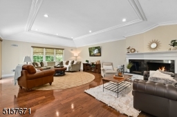 Room with hardwood floors, deep base and crown moldings, tray ceiling with deep moldings, recessed lights, wood burning fireplace with white millwork and a black marble hearth, glass sliders with direct access to the deck