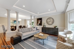 Living Room featuring hardwood floors with walnut inlay border, wainscotting, crown moldings, recessed lights, bay window, recessed ceiling with back lighting, and four majestic pillars separating the living room from the Dining Room